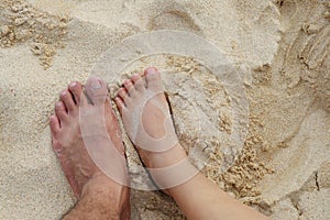 The feet of women and men stepping on the sand on the beach.