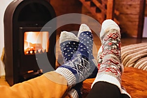 Feet in wool socks warming near fireplace in rustic cabin house. Cozy winter