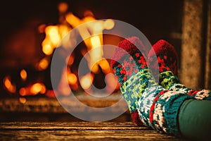 Feet in woollen socks by the fireplace. Woman relaxes by warm