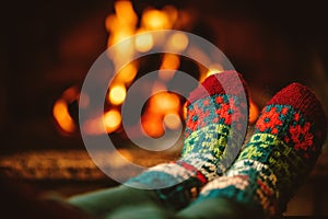 Feet in woollen socks by the fireplace. Woman relaxes by warm fi