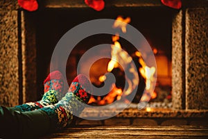 Feet in woollen socks by the fireplace. Woman relaxes by warm photo