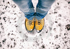 feet in yellow trekking boots on snow, a trip in winter, a picture from above