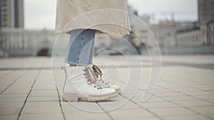 Feet of young Caucasian woman in casual clothes stomping on urban city square. Unrecognizable lady waiting outdoors on