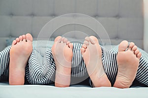 The feet of a young couple on the bed, closeup. Boyfriend and girlfriend lying in bed under blanket. Family bedroom