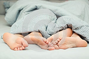 Feet of a young couple lying on the bed at honeymoon. Couple in love. Love lying in bed in hotel. Close up legs under stripes