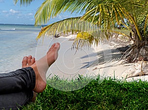 Feet of a young girl relaxing in the foreground against a Caribbean beach background. Blue sky and palm trees