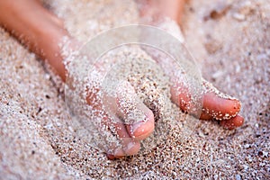 Feet of a young girl in the sand by the ocean closeup