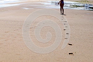 Feet of a young girl walk barefoot on a wet beach, leaving footprints in the sand