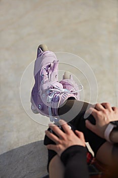 Feet of a young inline skater girl sitting on top of a ramp in a concrete skatepark. Aggressive in-line roller blader female