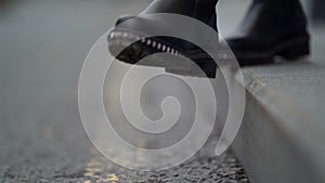 Feet of young woman on asphalt in city at cloudy autumn day, black leather shoes, closeup view