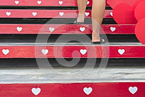 Feet of young woman walk up the stairs decorated with beautiful red and white hearts on occasion of Valentines Day festival of