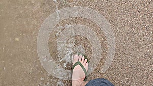 Feets of young man wearing flip flop sandals walking on the beach