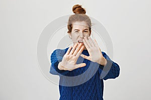 Feh, how gross, get it away. Studio shot of disgusted and displeased cute redhead female sister pulling palms towards