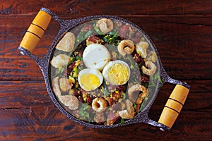 Feijao Tropeiro typical dish of Brazilian cuisine, made with beans, bacon, sausage, collard greens, eggs, on rustic wooden table