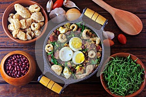 Feijao Tropeiro typical dish of Brazilian cuisine, made with beans, bacon, sausage, collard greens, eggs, on rustic wooden table