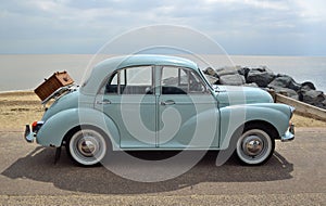 Classic Light Blue Morris Minor with picnic basket parked on seafront promenade.