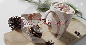 Feliz navidad text in red over pine cones, cinnamon and christmas hot chocolate with marshmallows