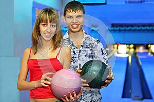 Fellow and girl stand with balls for bowling photo