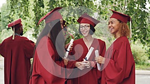 Fellow students are talking and laughing after graduation ceremony holding diplomae and wearing gowns and mortarboards