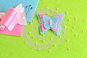 Felt butterfly, paper templates, thread, needle, pins, beads, blue and pink sheets on a green background. Sewing set, tutorial