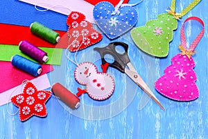 Felt Christmas ornaments. Christmas tree, heart, star, snowman crafts, scissors, sewing kit, felt sheets on blue wooden background