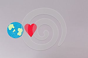 A felt-cut symbol of the planet earth and a red heart. Gray background. Flat lay. Copy space. The concept of environmental
