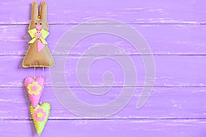 Felt Easter bunny decorated with bow, buttons and hearts isolated on purple wooden background with copy space for text