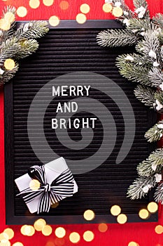 Felt or letter board with phrase merry and bright, box with present and fir tree spruces on bright red paper textured background.