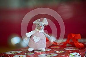 A felt mouse Christmas tree decoration sitting on a red wrapped present with silver baubles in the red background