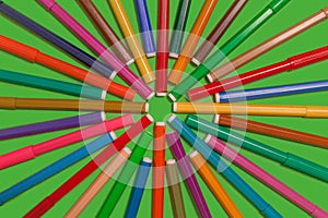 Felt pens lying on a green surface forming a shape of cirlcle