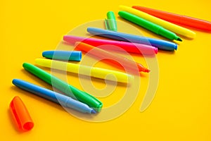 Felt-tip pens on a yellow background with copy space, set of new bright plastic opened colored felt pens near the caps