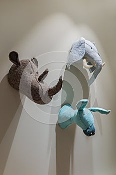 Felted animals toys hanging on the wall. Heads of donkey, rhinoceros and elephant on gray wall. Emulation of trophies