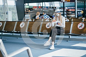 Female 25-35 years old, wearing a hat and a protective mask, sits at the check-in counters in the airport terminal