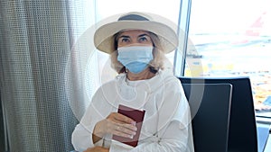 Female 50-55 years old, wearing a hat and a protective mask, sits at the check-in counters in the airport terminal