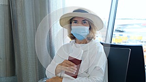 Female 50-55 years old, wearing a hat and a protective mask, sits at the check-in counters in the airport terminal