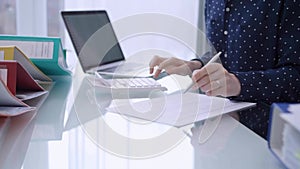 A female accountant is using a laptop computer and calculator to calculate taxes at a glass desk in the office