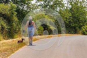 Female adult hiker walking with her dog on left side of a country road