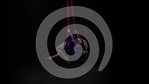 Female aerial gymnast performing on a red silk in a black background. Exciting acrobatic show. Slow motion. 141