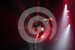 Female aerialist do stretching split on aerial silks with high heels backlit in red light. Face to the right