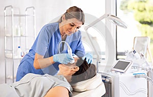 Female aesthetician administering high frequency ultrasound facial procedure on woman