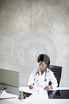 Female African American doctor wearing white coat with stethoscope sitting behind desk in office