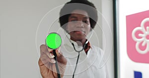 Female African American medical professional displaying stethoscope with green screen. Woman doctor holding stethoscope