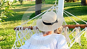 female age 50-60 in a straw hat is resting in a hammock around the palm trees and enjoying the tranquility and