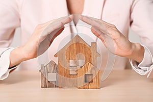 Female agent covering wooden houses at table. Home insurance