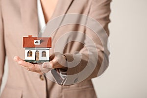 Female agent holding house model on light background, closeup.