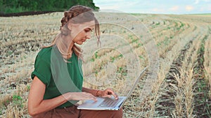 Female agronomist using laptop while examining field