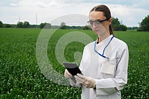 a female agronomist in a white coat checks the growth of plants in the field. A biologist in the field checks the readings of