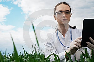 a female agronomist in a white coat checks the growth of plants in the field. A biologist in the field checks the readings of