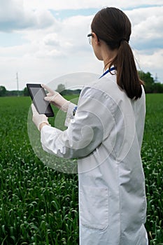 a female agronomist in a white coat checks the growth of plants in the field. A biologist in the field checks the readings of