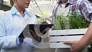 Female agronomy specialist working tablet talking to hothouse worker with plants